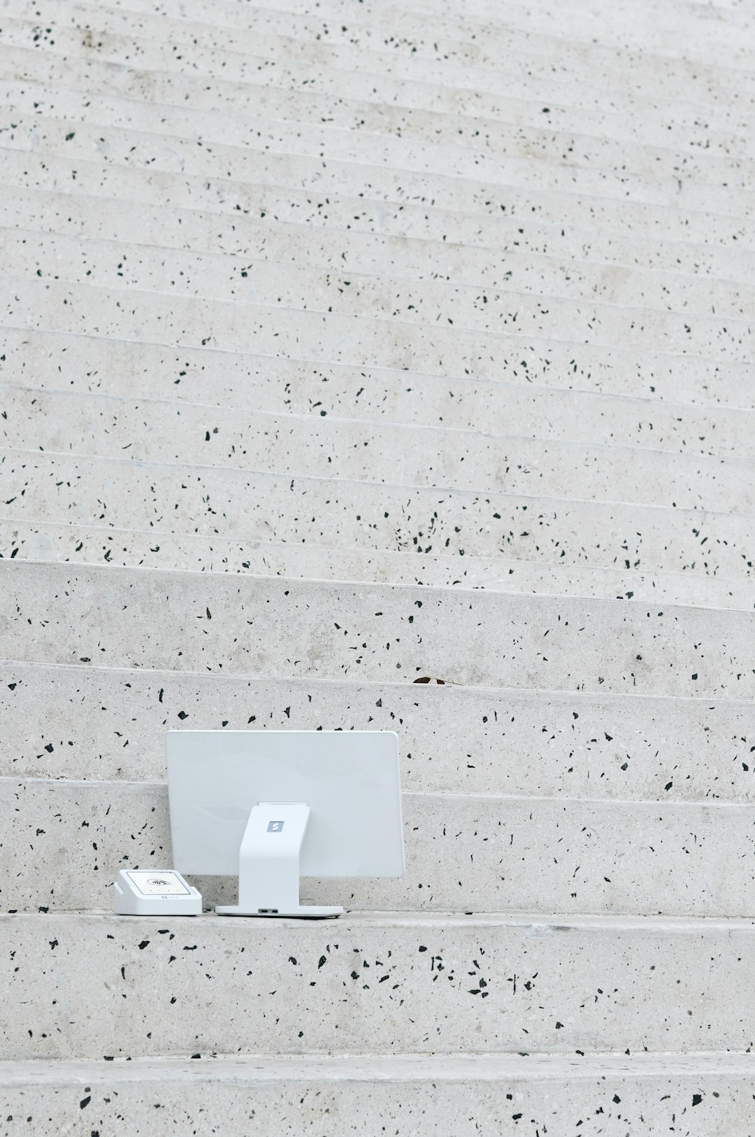 The SumUp POS Lite is seen placed on the steps of the Pyramid of Tirana, creating a striking contrast between modern payment technology and the iconic concrete architecture. The minimalistic design of the device stands out against the raw, textured stone, blending innovation with history in this unique setting.